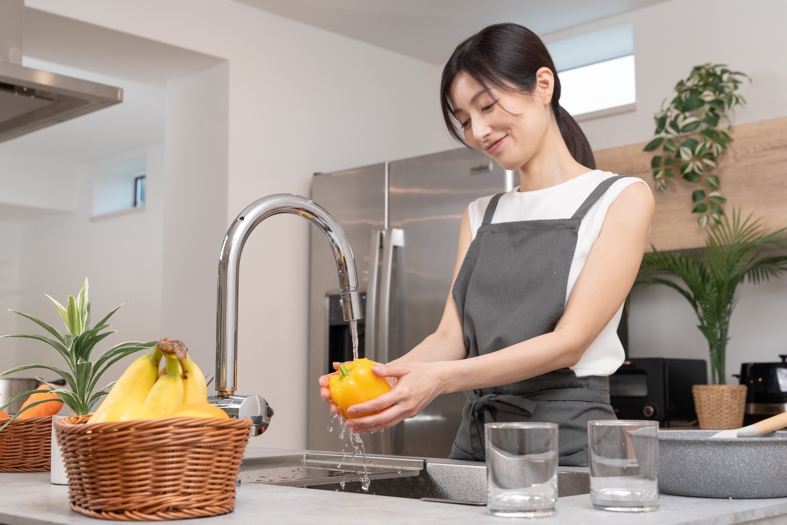 キッチンで浄水を使い、野菜を洗う女性